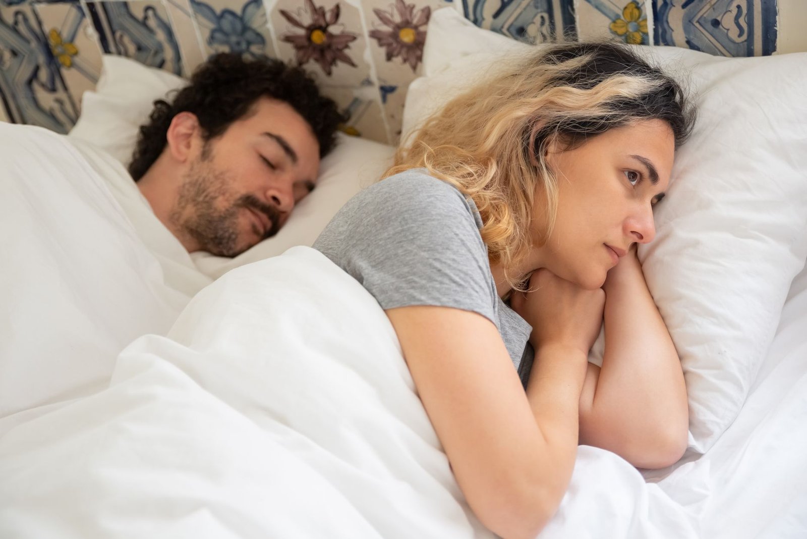 A woman lying awake in bed at night beside a sleeping partner.